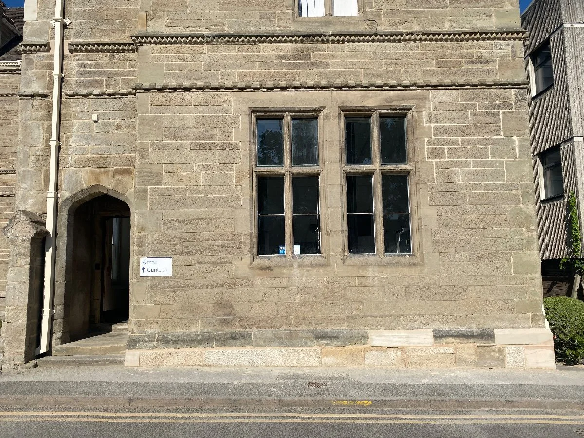 Arched doorway of an old stone building with two large windows to the right of the doorway.