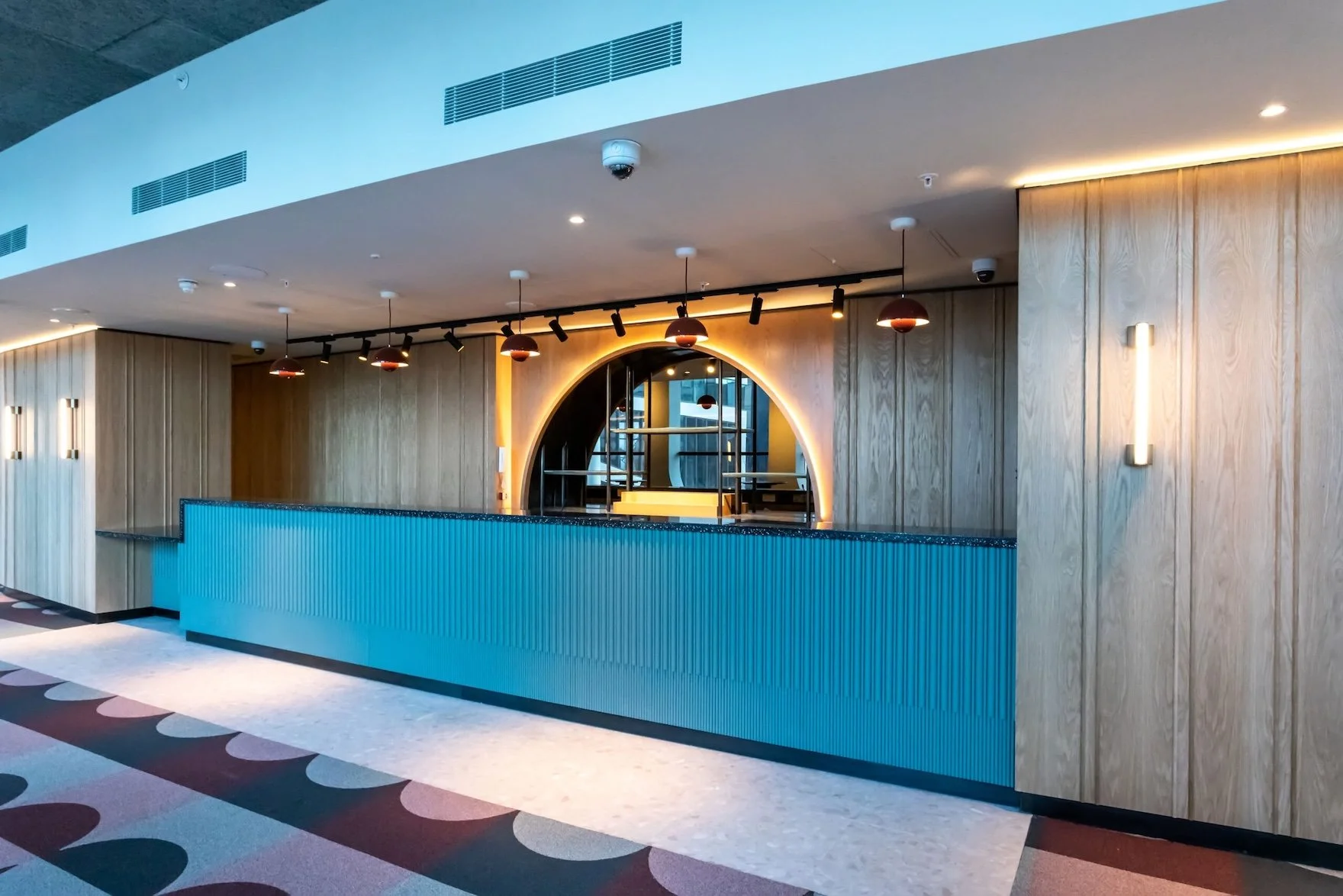 Large, empty leisure venue with a blue-panelled long desk built into an alcove, with wooden effect walls either side.