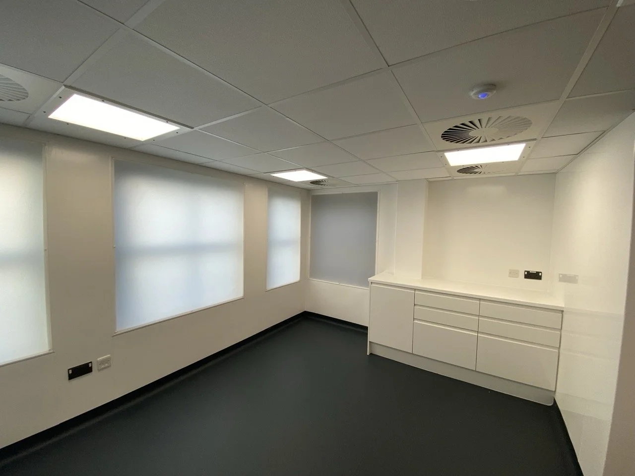 Clinical white toilet area in a health centre with a row of white cupboards.