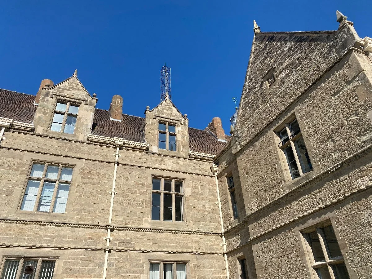 Closeup of a section of a large two-story stone building. Blue sky sits above the building.