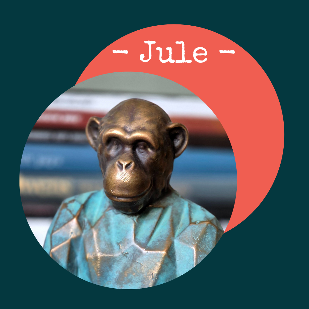Statue de singe humain en bronze portant un vêtement bleu, avec un fond de livres et un graphique rouge marqué 'Jule'.