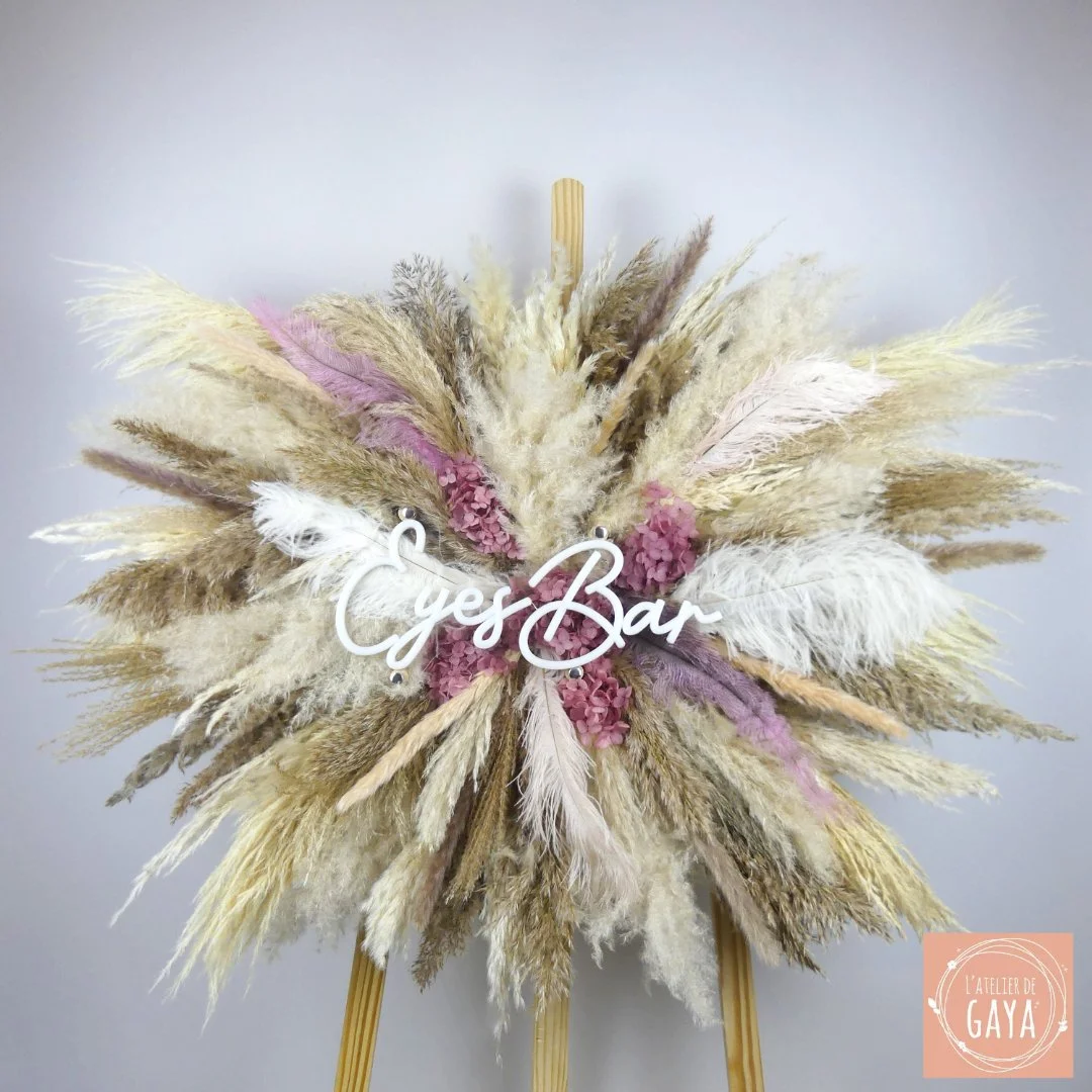 Décoration florale avec des pampas, des fleurs et un panneau en bois indiquant 'Cyes Bar'.