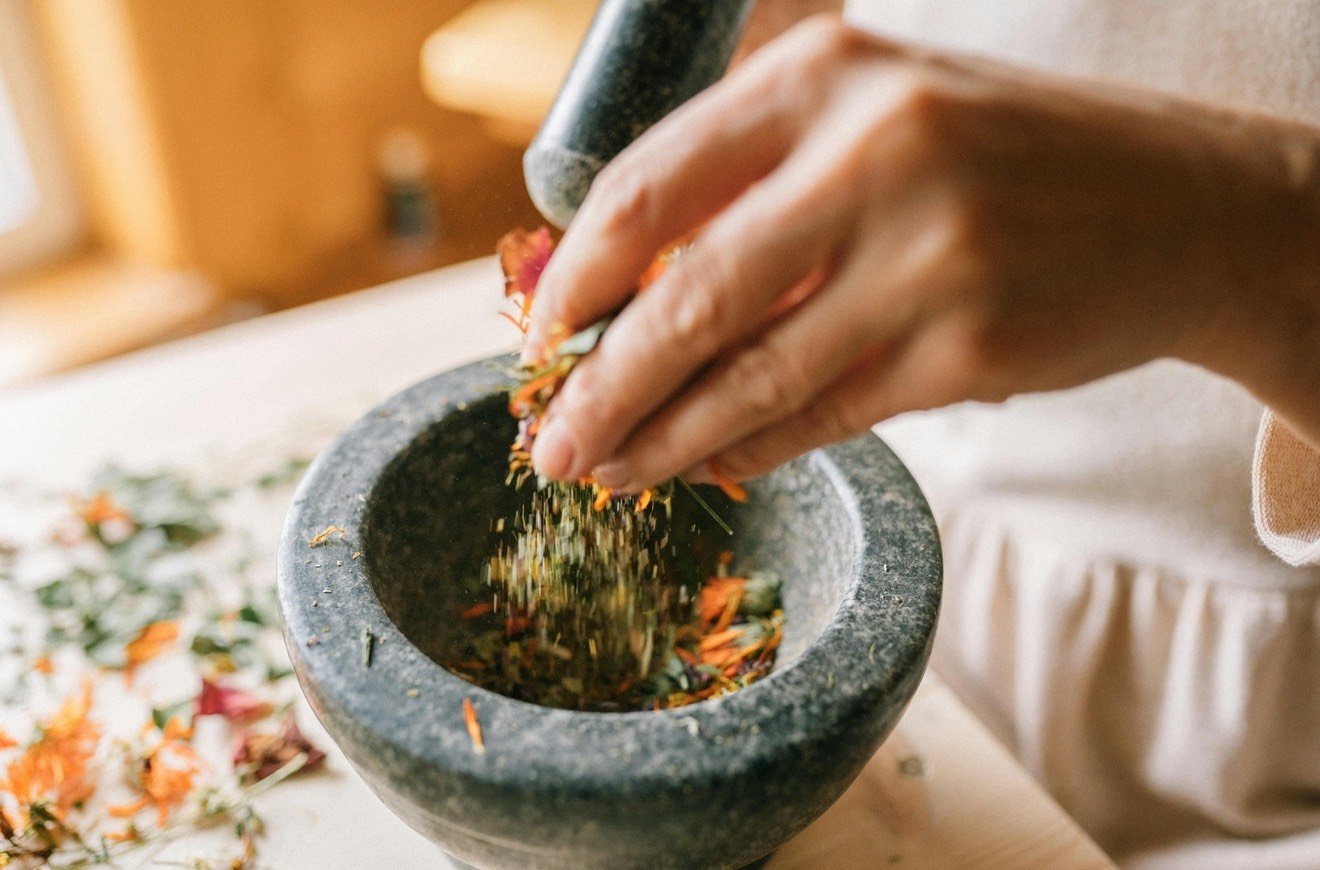 Person grinding dried herbs or flowers in a stone mortar with a pestle.