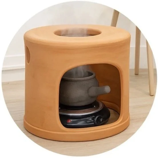 A wooden stove with a tea kettle on a hot plate, steam rising from the kettle, in a room with wooden flooring and white walls.