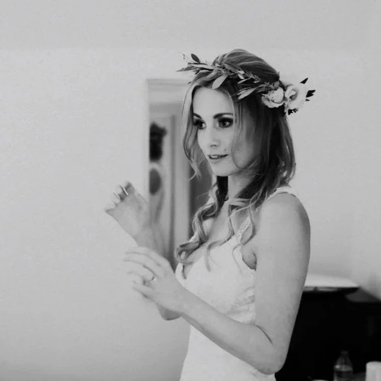 A woman wearing a flower crown takes a selfie with her phone in a mirror.