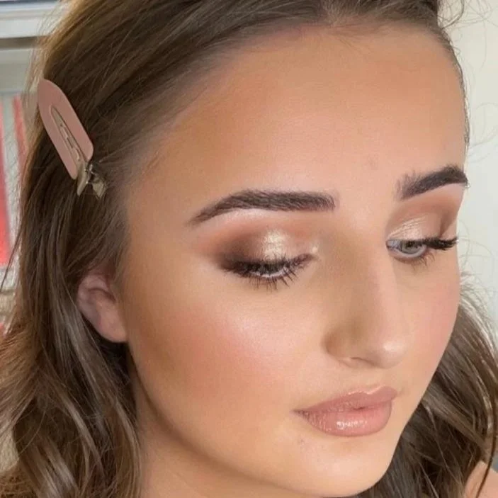 Close-up of a woman with light makeup, including shimmery eyeshadow and glossy lips, with hair clipped back