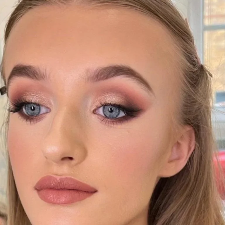 Close-up of a woman's face with makeup, including eye makeup, foundation, and lipstick, and blue eyes.