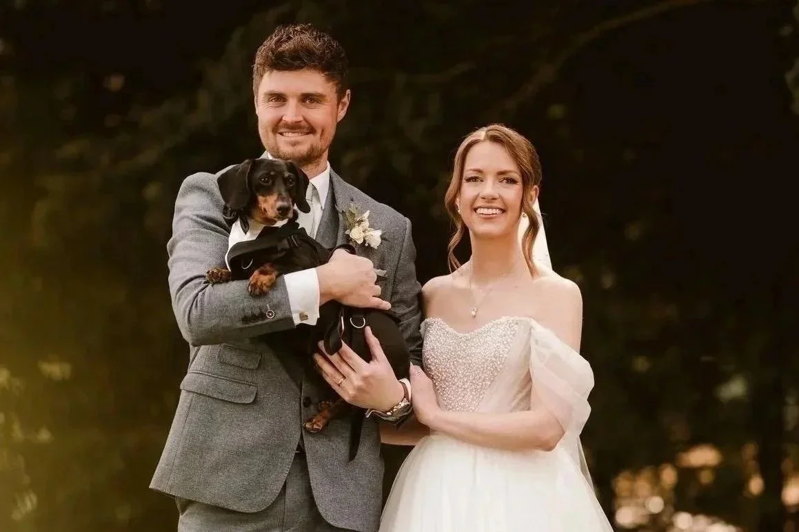 Another gorgeous wedding makeup wedding client in  wedding attire standing outdoors with a small dog, smiling at the camera.