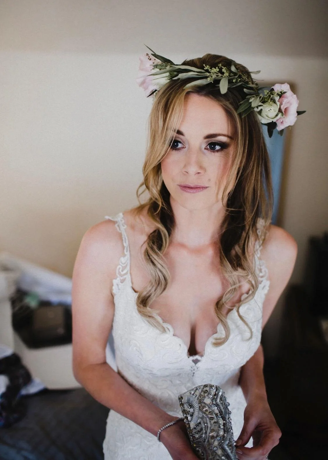 A woman in a white lace wedding dress with a floral crown on her head, holding a beaded clutch purse.