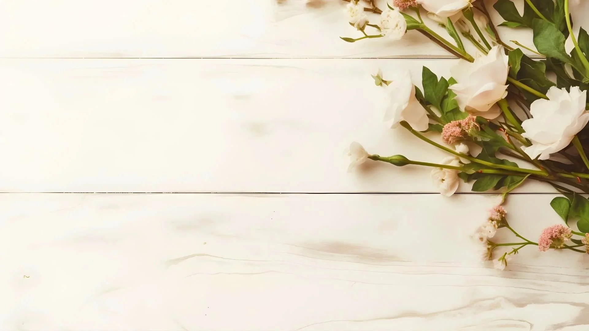 Arrangement of white and pink flowers with green leaves on a white wooden surface.
