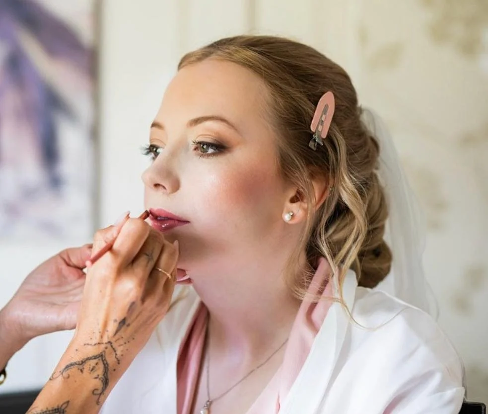 A woman getting her makeup applied, with her hair pinned back and secured with a pink hair clip.
