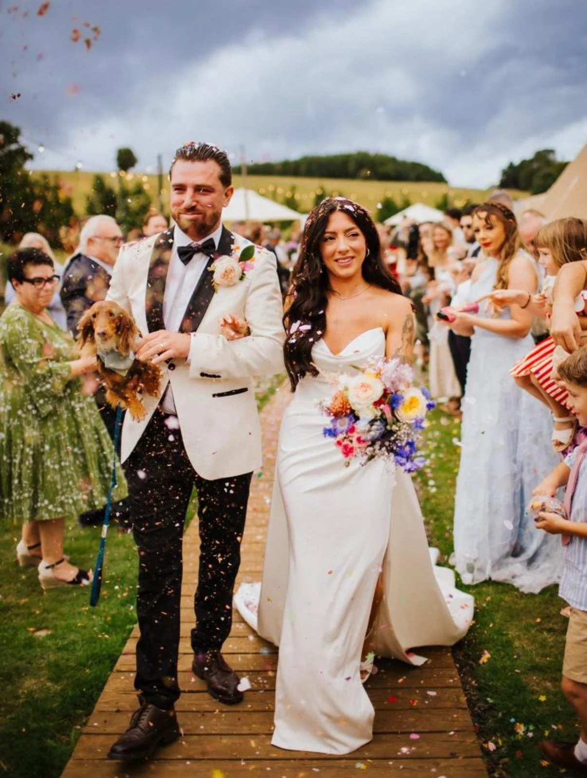 Bride and groom walking down the aisle at their outdoor wedding ceremony, with guests on either side throwing confetti.