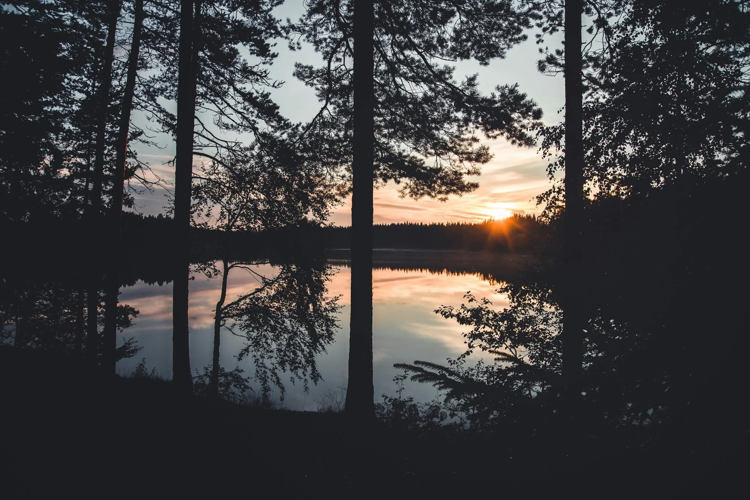 A serene sunset view over a lake, framed by tall trees with reflections on the water.