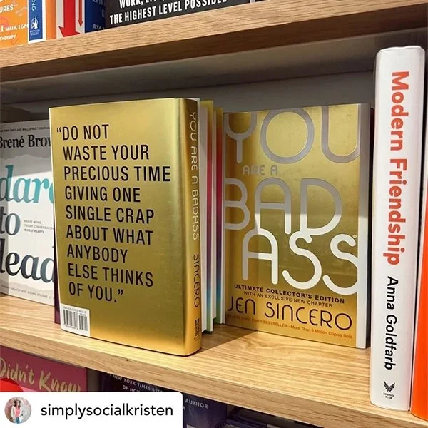 Books on a wooden bookshelf, including 'You Are a Badass' by Jen Sincero and 'Modern Friendship' by Anna Goldenberg.