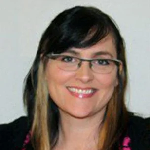 A woman with dark hair, glasses, and a bright smile, wearing a black top.