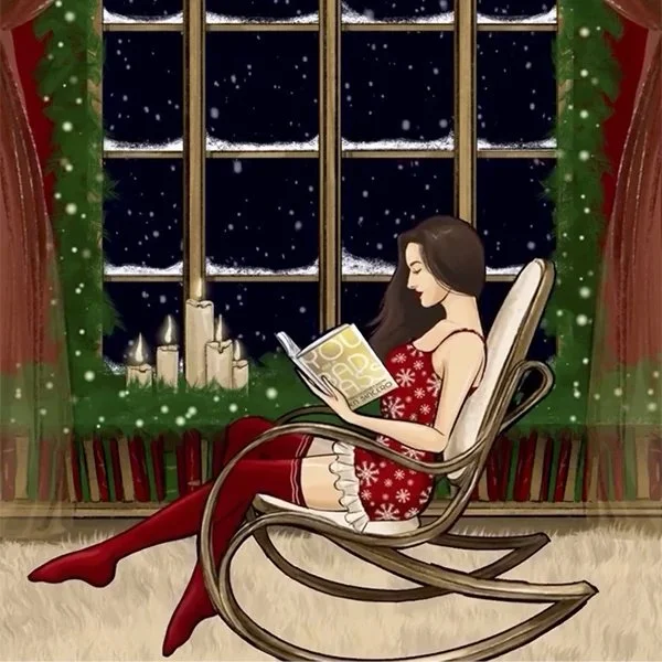 Woman in Christmas pajamas reading a book while sitting in a rocking chair by a window with snow falling outside, decorated with candles and holiday greenery.