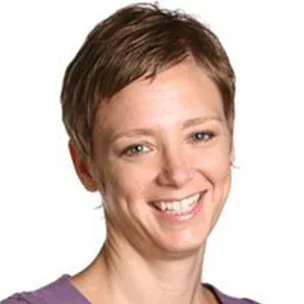Close-up of a woman with short brown hair and a purple shirt, smiling.