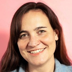 Close-up of a smiling woman with shoulder-length brown hair against a pink background.