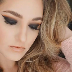 Close-up of a woman with blonde hair and makeup, looking down with eyes closed.