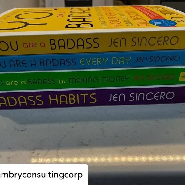 A stack of four books with colorful covers. Each book has motivational titles with the author Jen Sincero. The titles are: "You are a BADASS," "You ARE A BADASS EVERY DAY," "You are a BADASS at MAKING MONEY," and "BADASS HABITS."