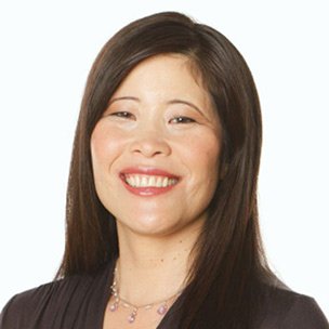A smiling woman with straight dark hair, wearing a black top and a necklace, against a plain white background.