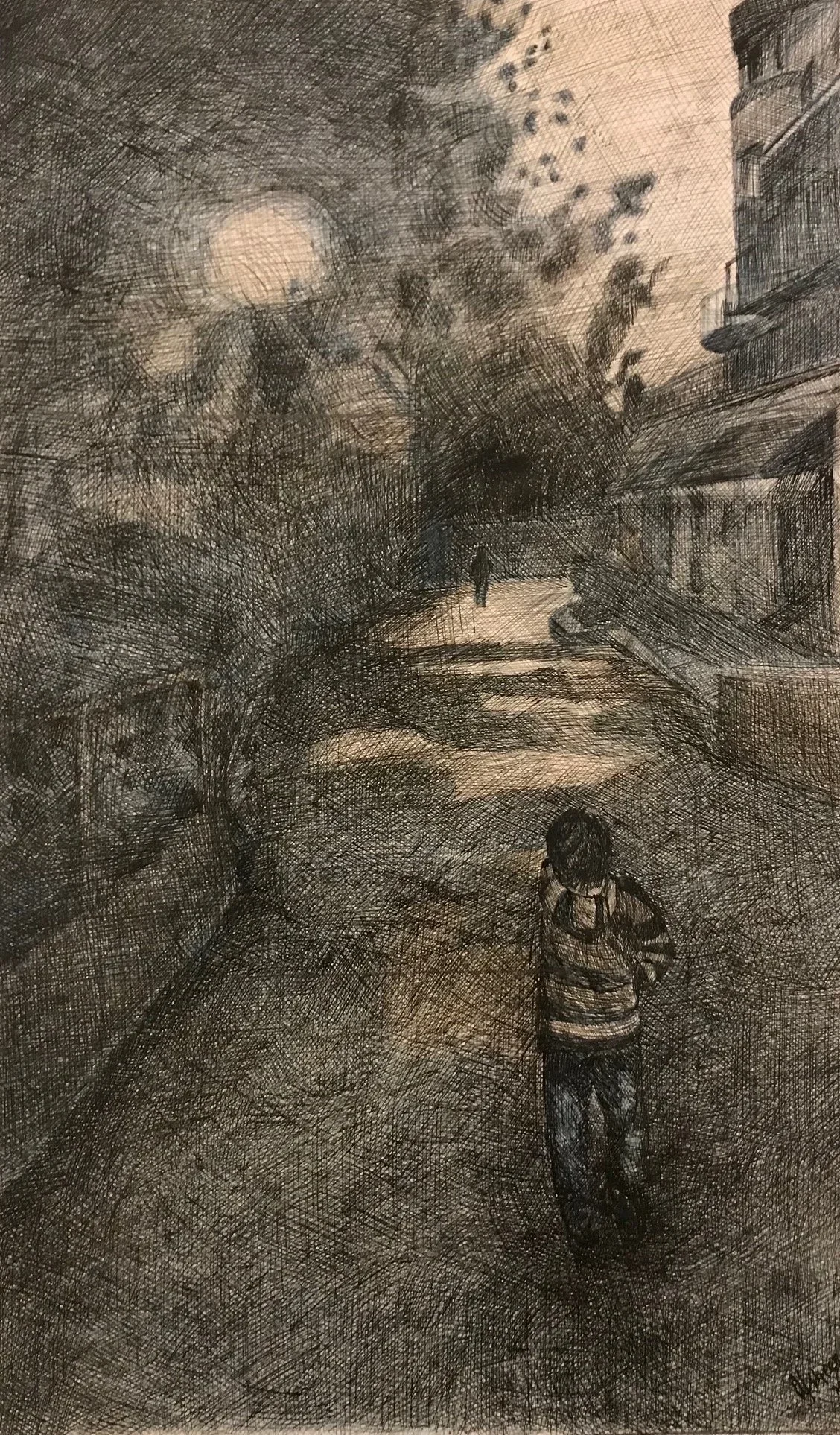 A detailed black and white sketch of a city street during evening or night. In the foreground, a young child with glasses and a striped shirt is walking away from the viewer. Further along the street, a person is walking in the distance. On the left, trees with bare branches and a lamp post are visible. On the right, buildings with balconies and windows line the street. The moon is shining through cloudy skies, casting light over the scene.