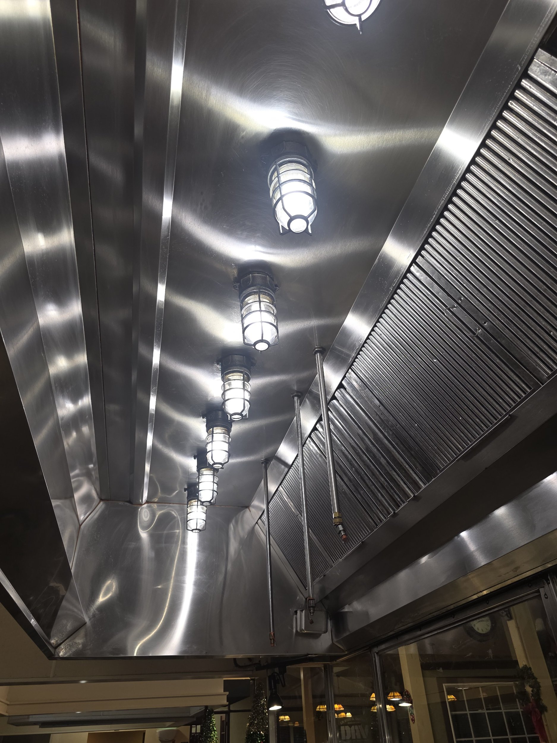 Ceiling with built-in fluorescent lights and a stainless steel exhaust hood in a commercial kitchen or restaurant.