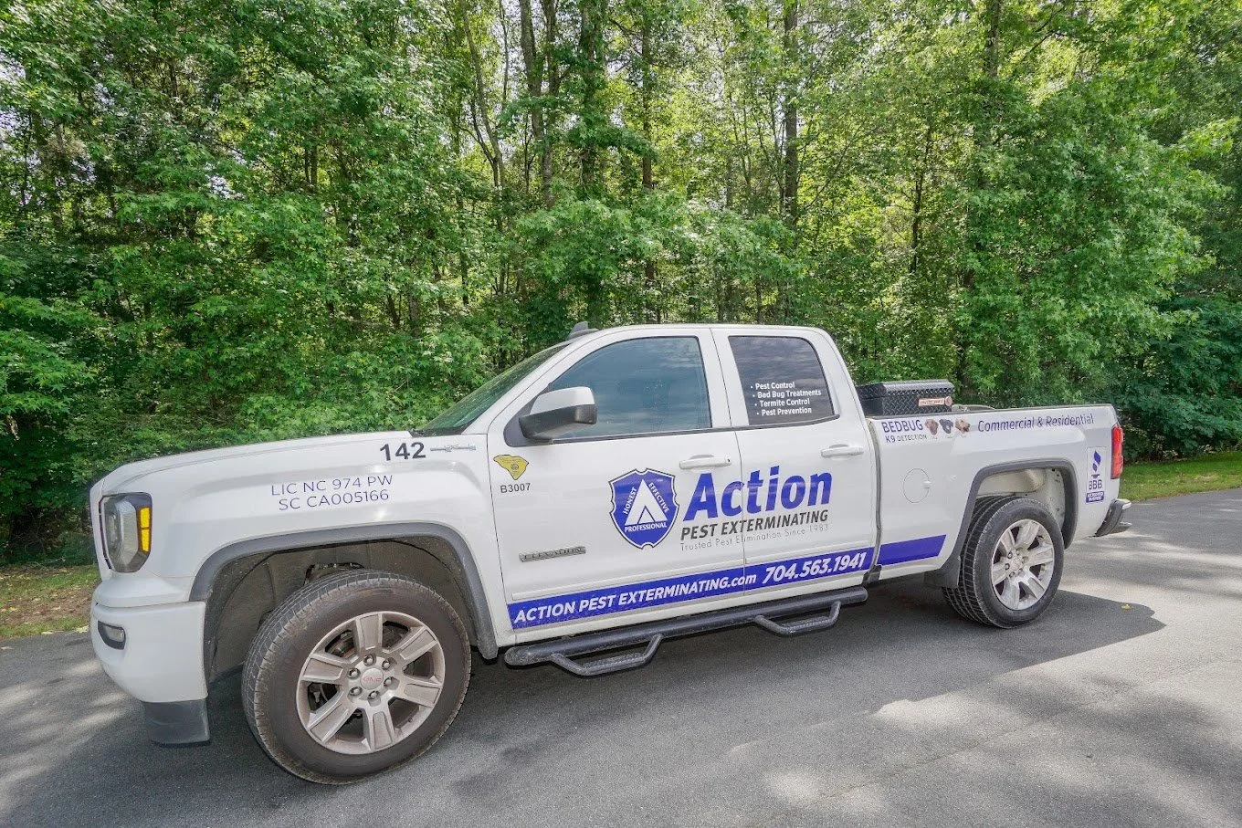 White pest control truck parked on a paved road with green trees in the background. The truck has signage for Action Pest Exterminating, including contact information and pest treatment services.
