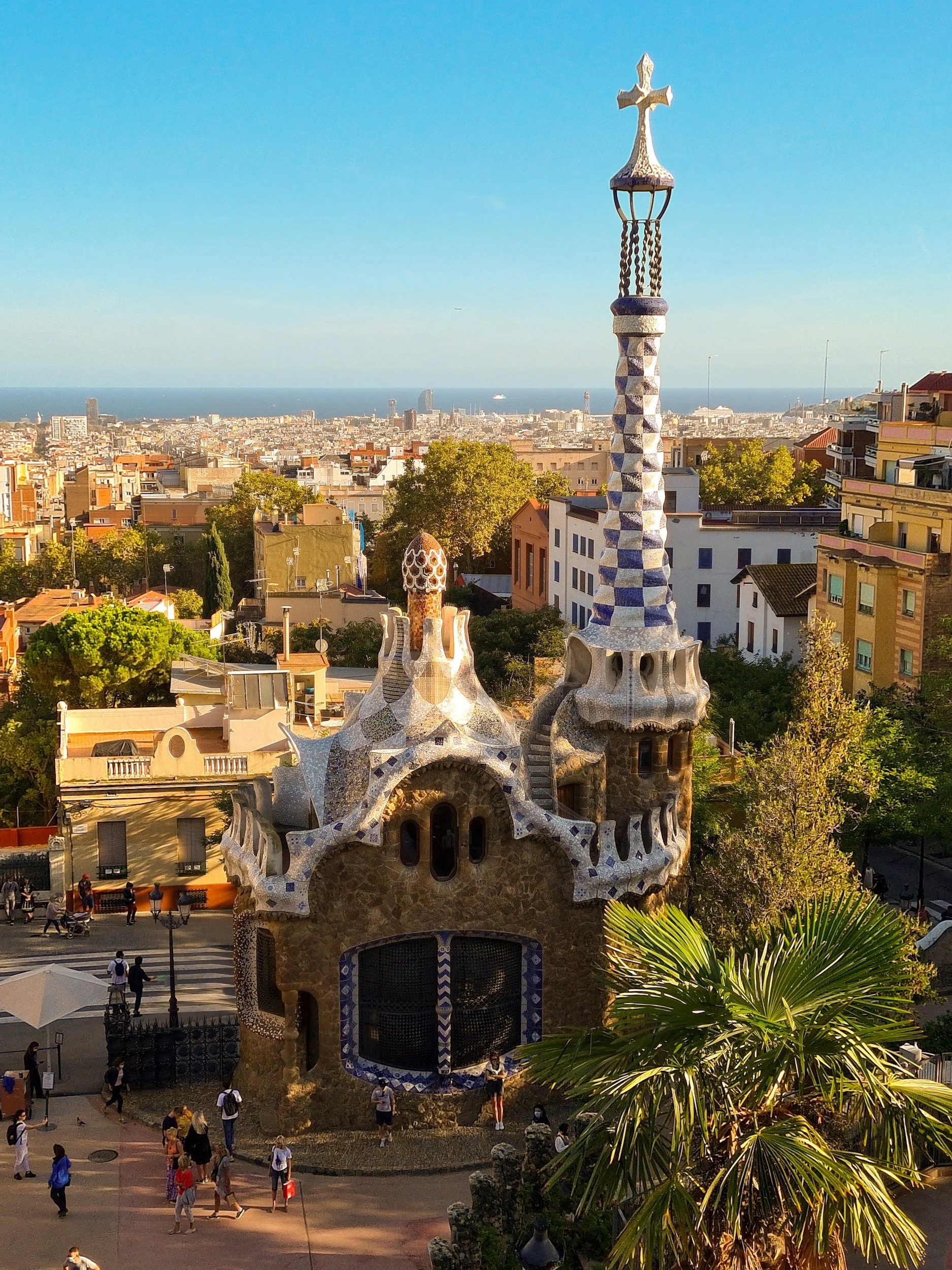 Colorful building with whimsical, mosaic-covered architecture in Park Güell, Barcelona, with cityscape and ocean in the background.
