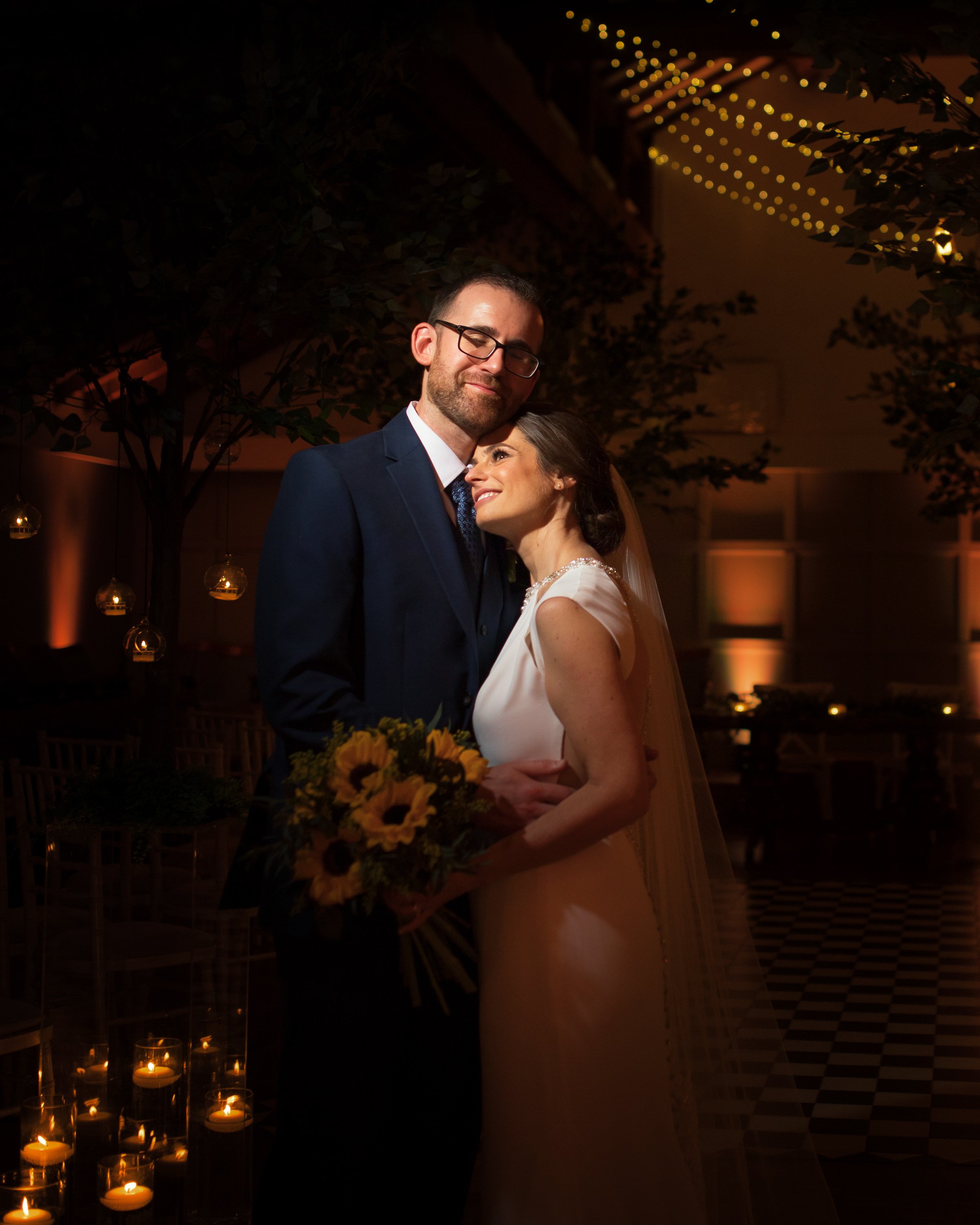 A bride and groom sharing an intimate moment at their wedding reception, with candles and soft lighting in the background.