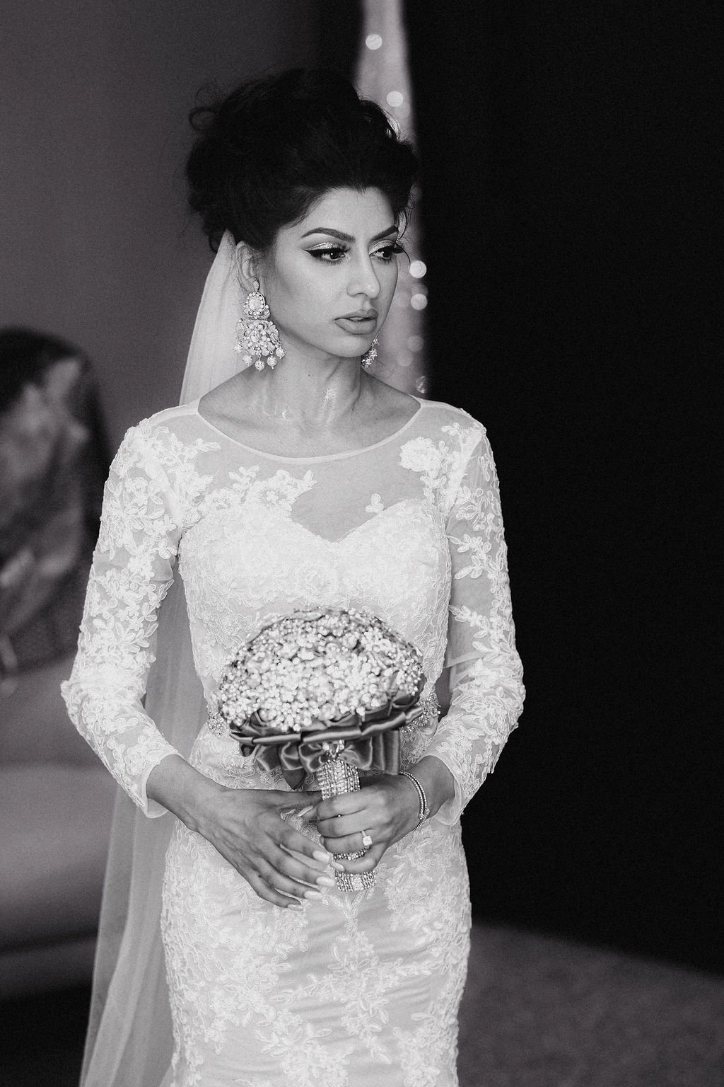 Black and white photograph of a bride in a long sleeve lace wedding dress holding a bouquet of flowers at her wedding.