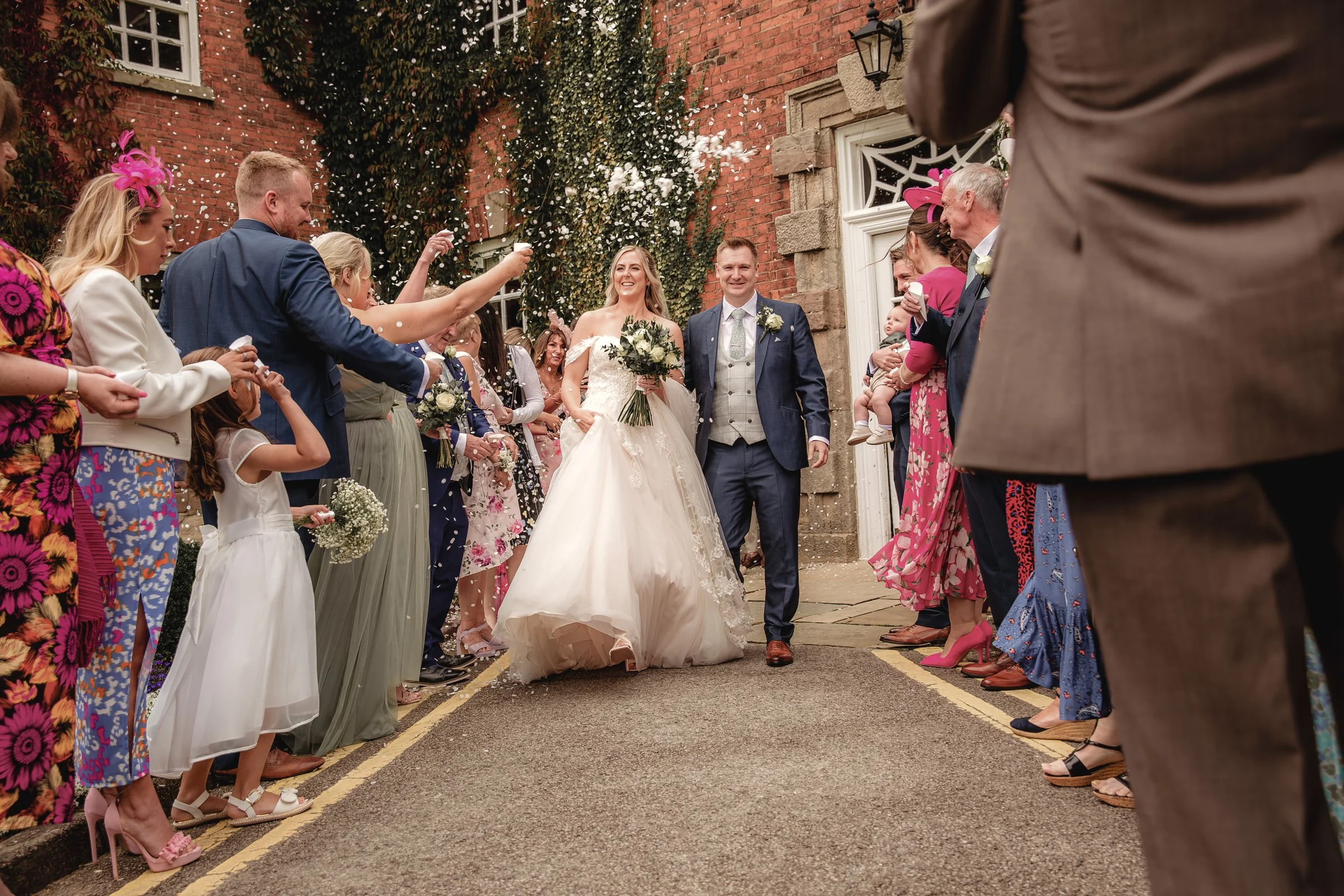 Bride and groom walking out of a building as family and friends celebrate with confetti and cheers.