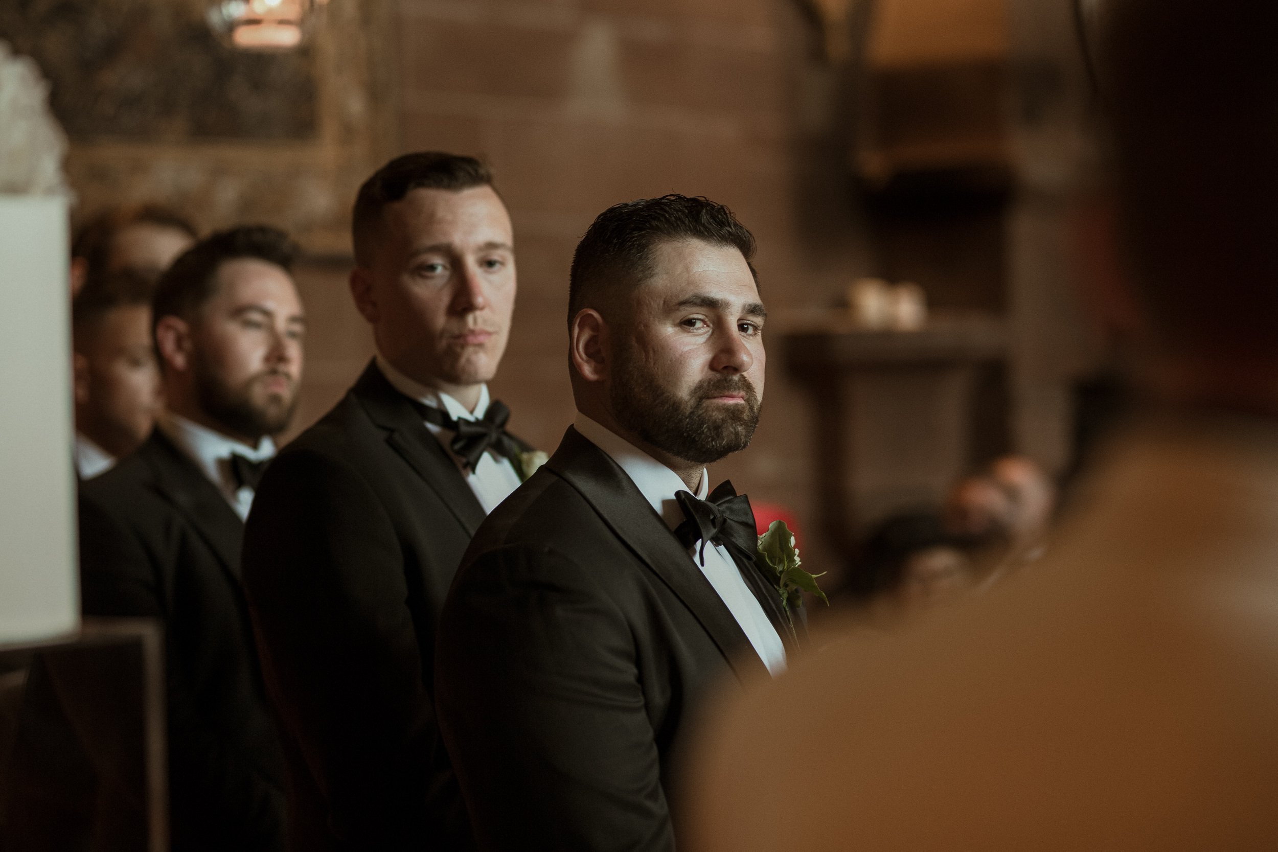 Groom and groomsmen in tuxedos at a wedding ceremony.