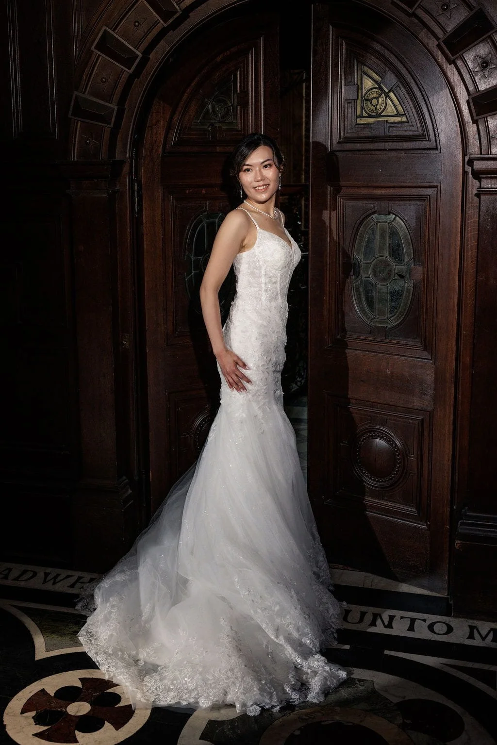 A woman in a white wedding gown standing in a doorway with dark wood paneling.
