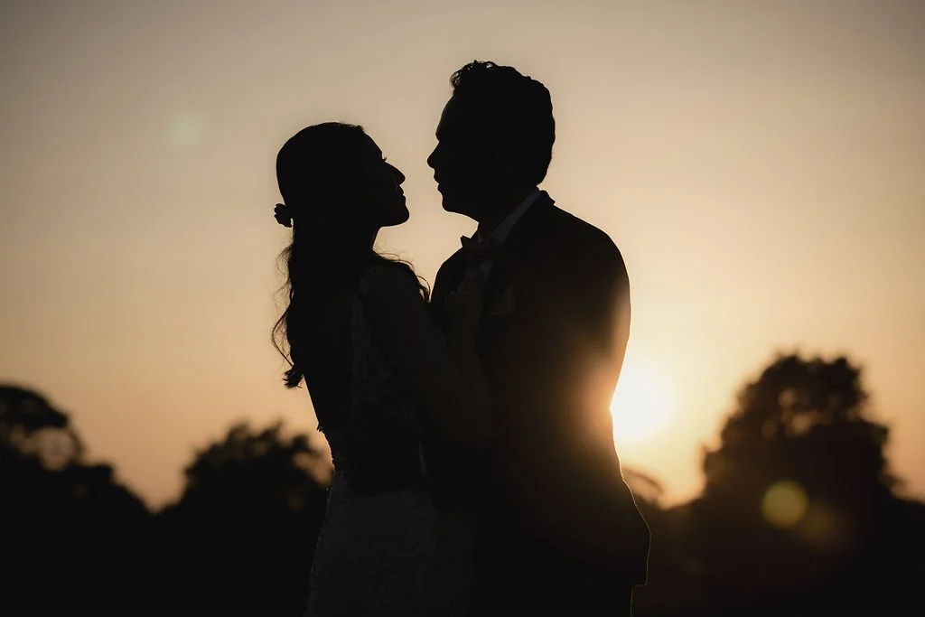Silhouette of a couple embracing during sunset with trees in the background.