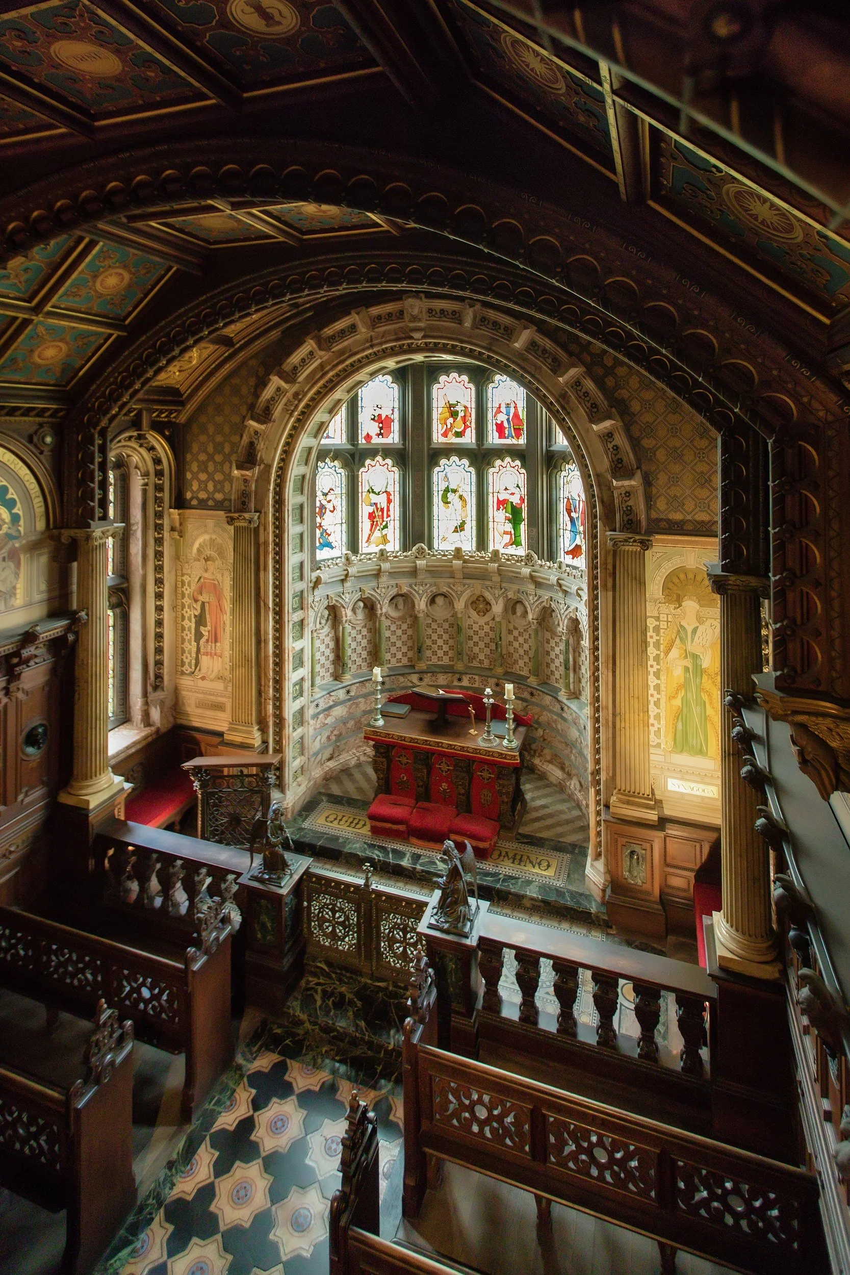 Interior of a church or chapel with ornate woodwork, stained glass windows, and religious artwork.