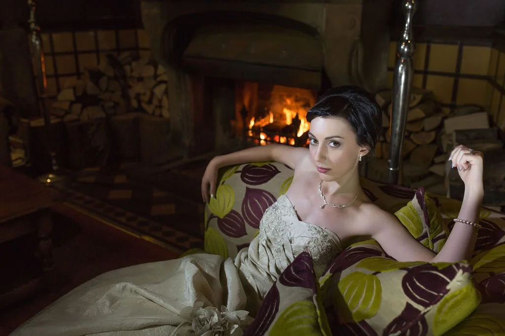A woman in a strapless dress sitting on a sofa in front of a fireplace.