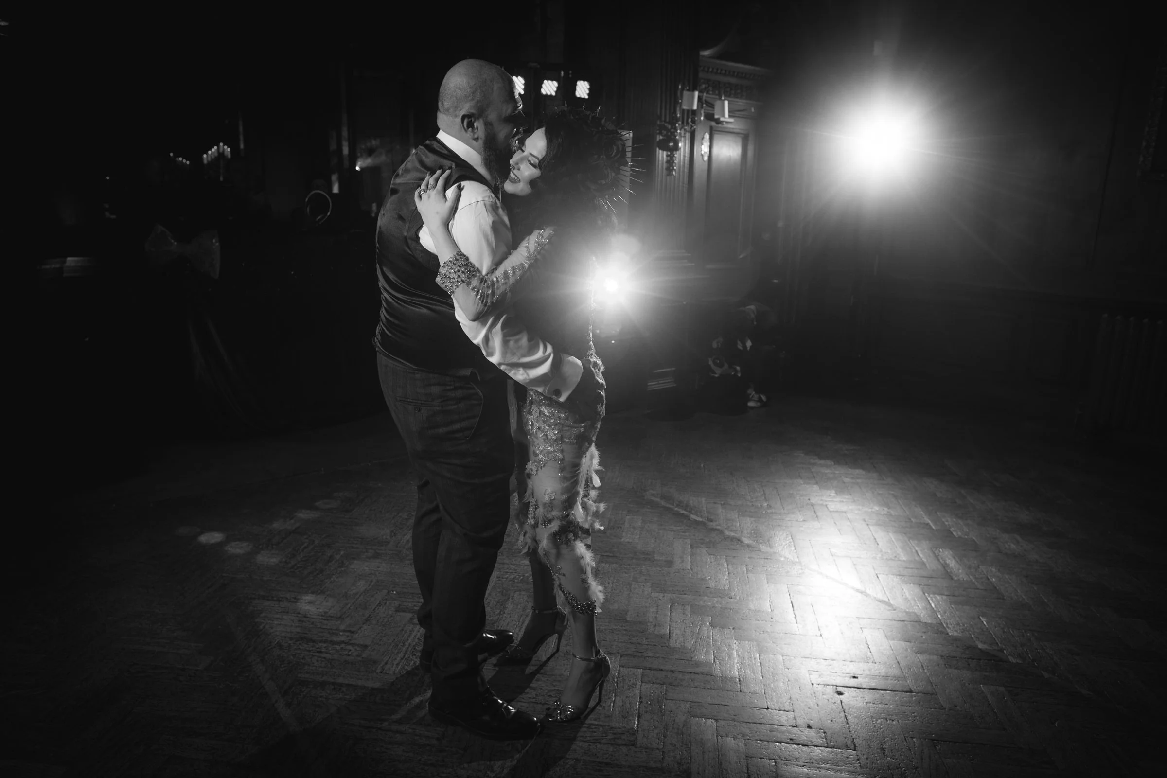A couple dancing closely in a dimly lit room with a bright light source behind them.