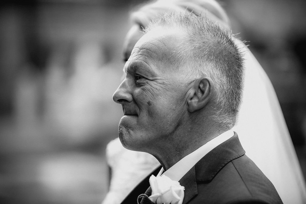 A side profile of a smiling man in a suit with a boutonniere, likely at a formal event or wedding.
