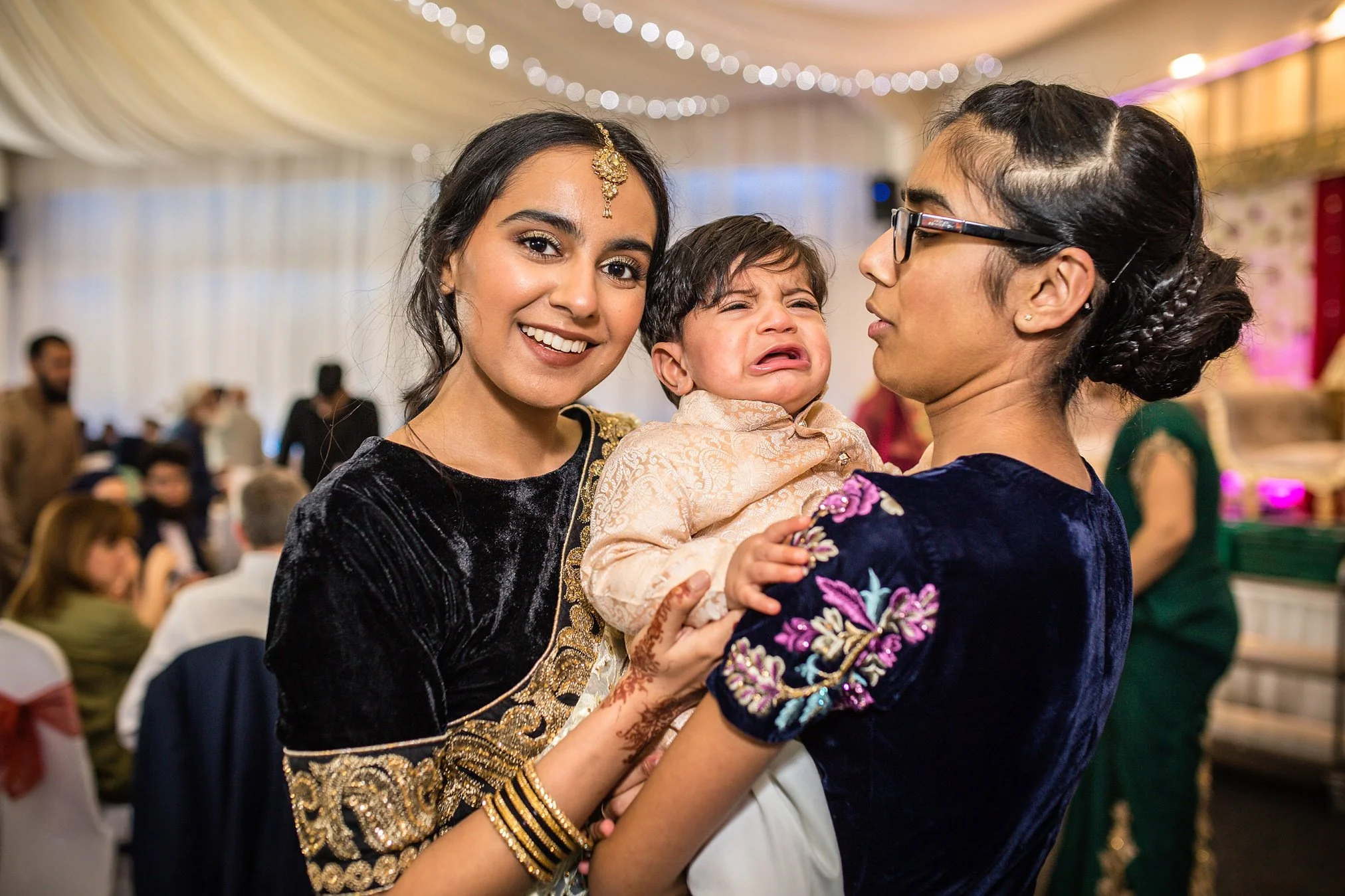 Two female wedding guests holding a crying baby boy in the wedding breakfast room.