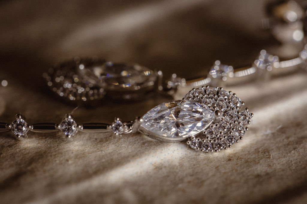 Close-up of a silver necklace with diamond-like stones resting on a textured surface.
