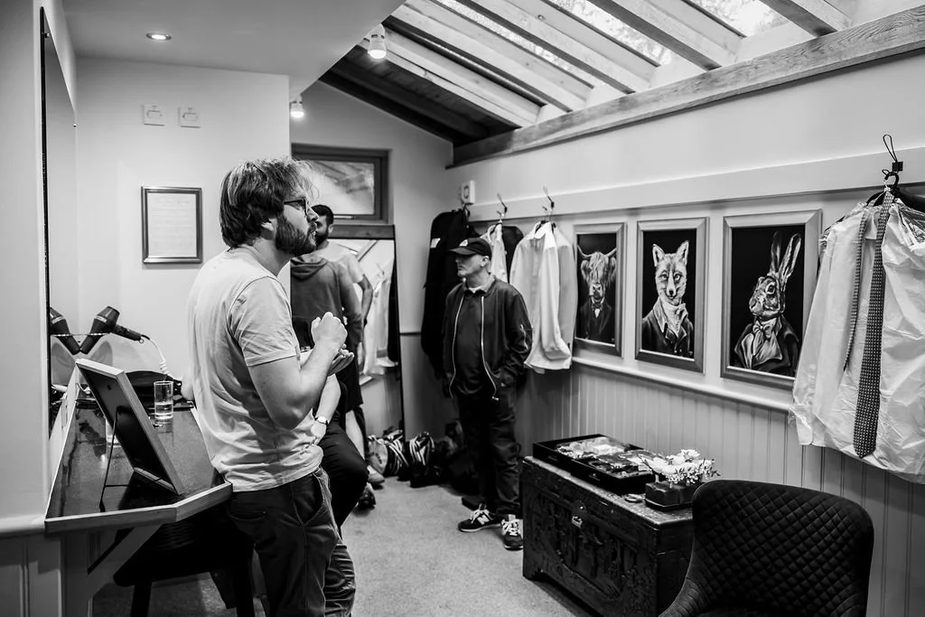 People in a room with animal portraits, jackets on the wall, and casual clothing, engaging in conversation.