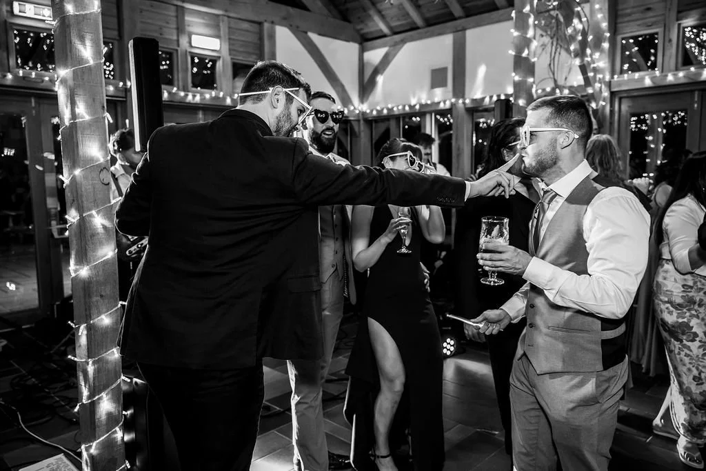 People dancing and socializing at a party, with string lights and large windows in a decorated venue.