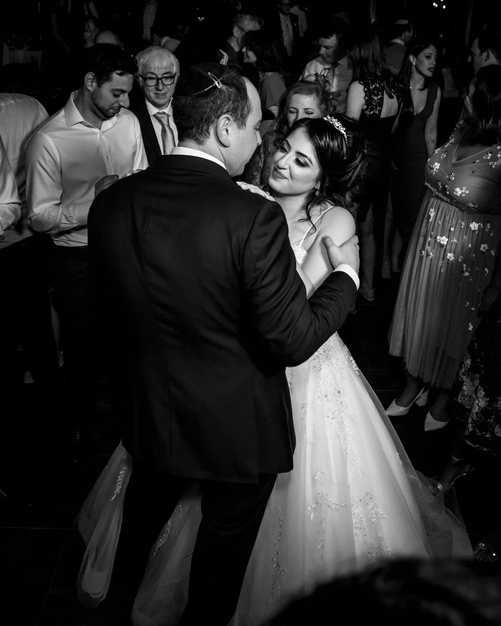 A bride and groom dancing at their wedding reception, surrounded by guests.
