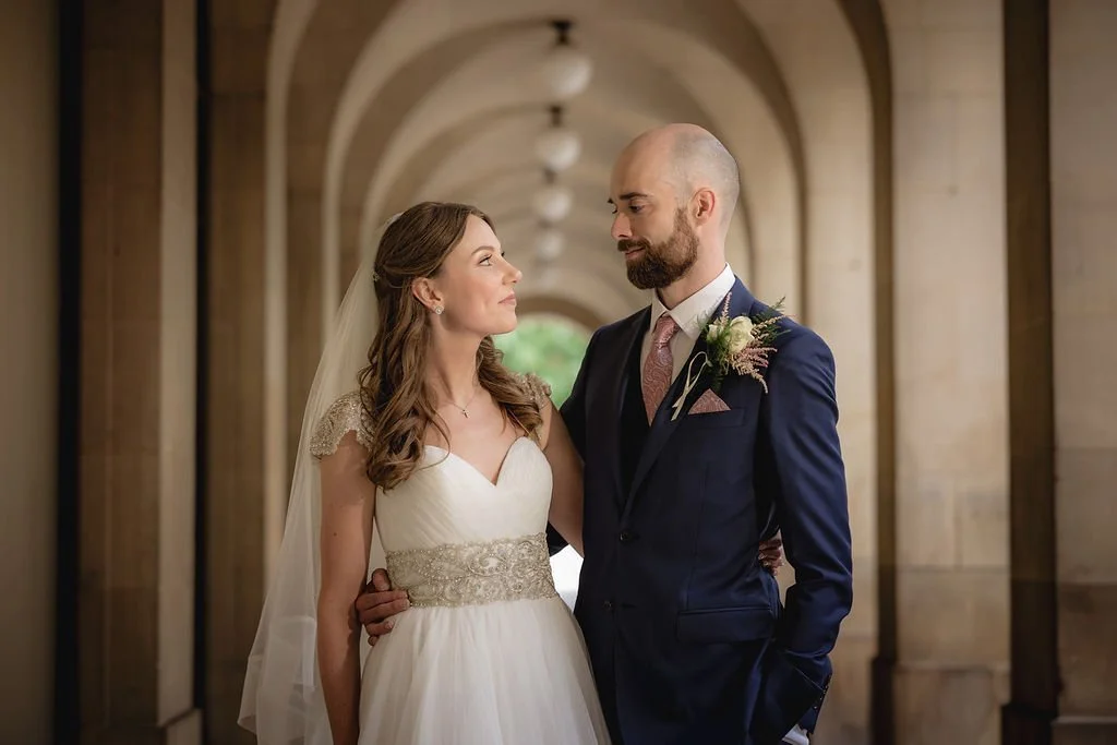 A bride and groom standing close together in a corridor with arched doorways, looking at each other during their wedding celebration.