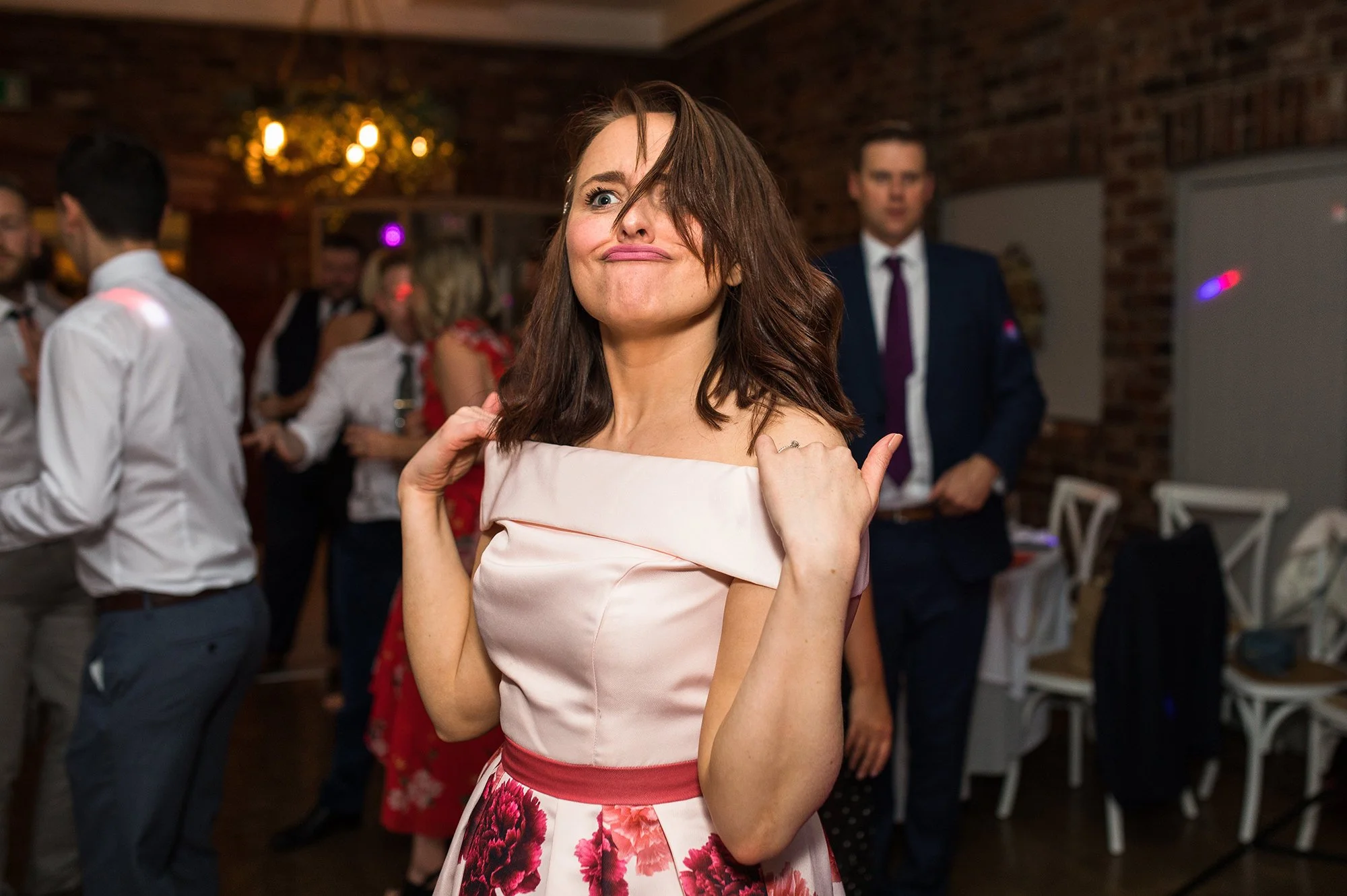 Woman in a floral dress making a humorous face at a social gathering or party.