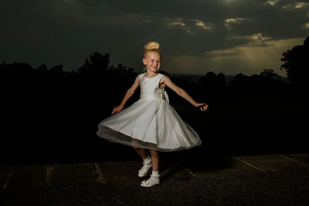 A young girl in a white dress dancing outdoors during sunset with trees in the background.