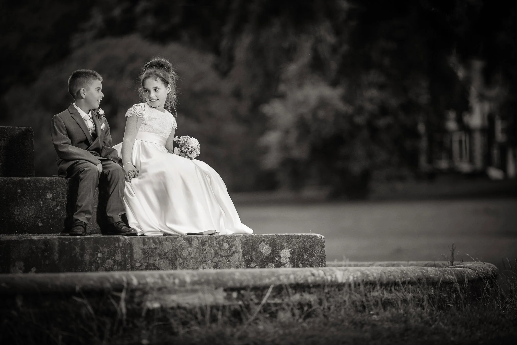 Little boy and girls sat outside on stone steps pretending to be a bride and groom.
