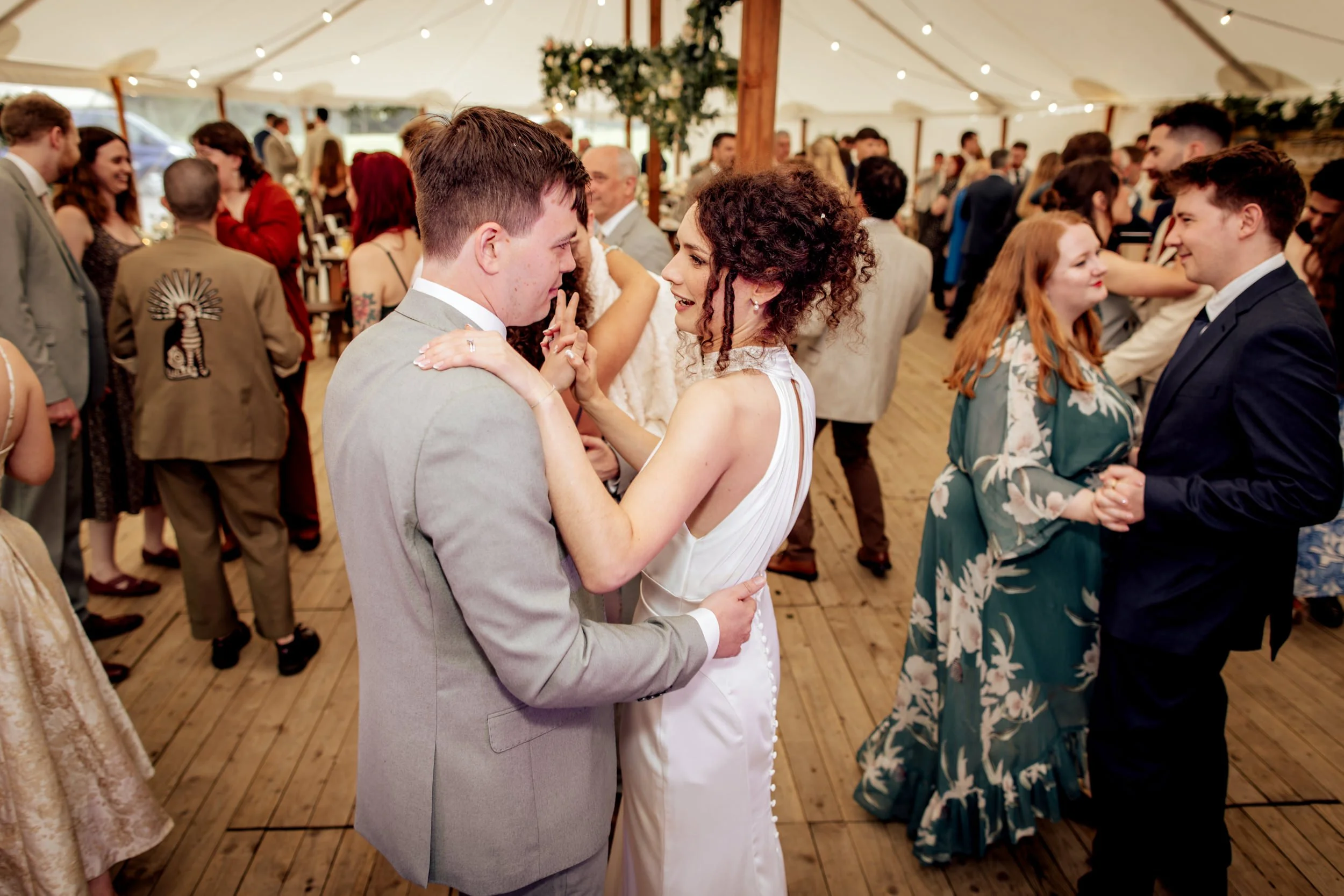 A bride and groom dance closely at their wedding reception surrounded by guests in a decorated tent.