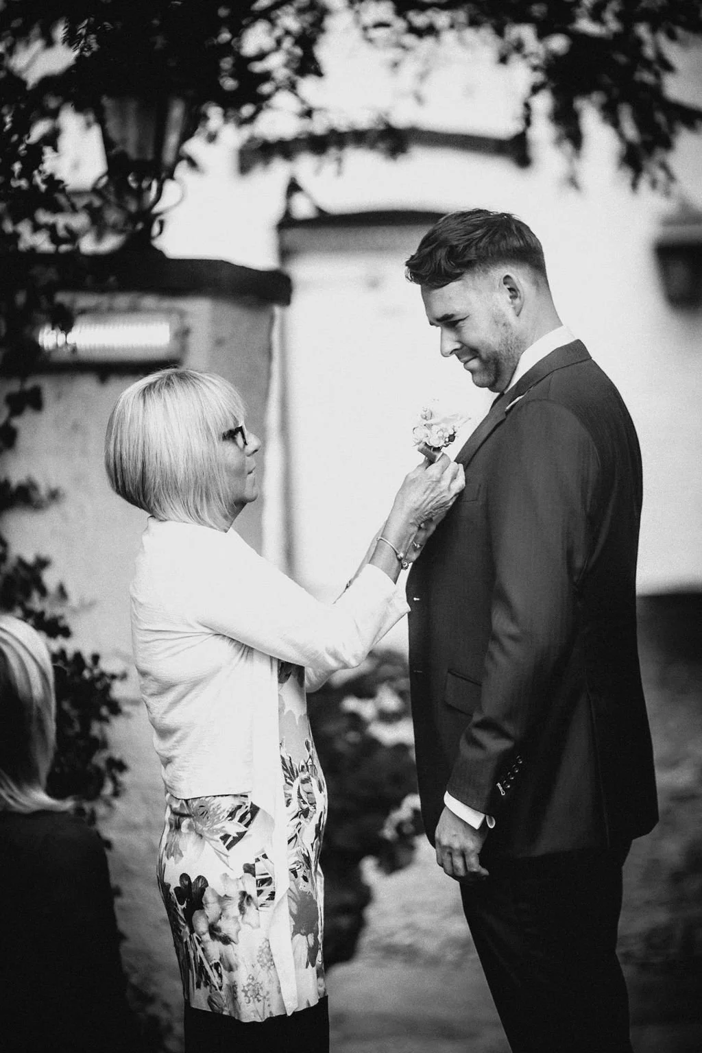 An elderly woman pinning a boutonniere on a man's suit jacket during a wedding ceremony.